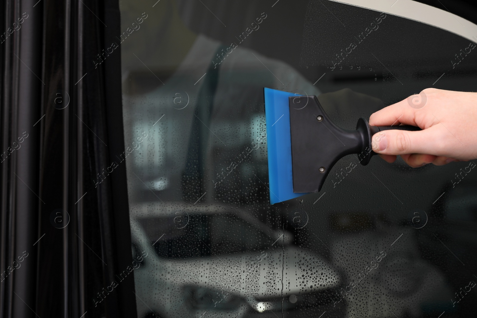 Photo of Worker washing tinted car window in workshop, closeup