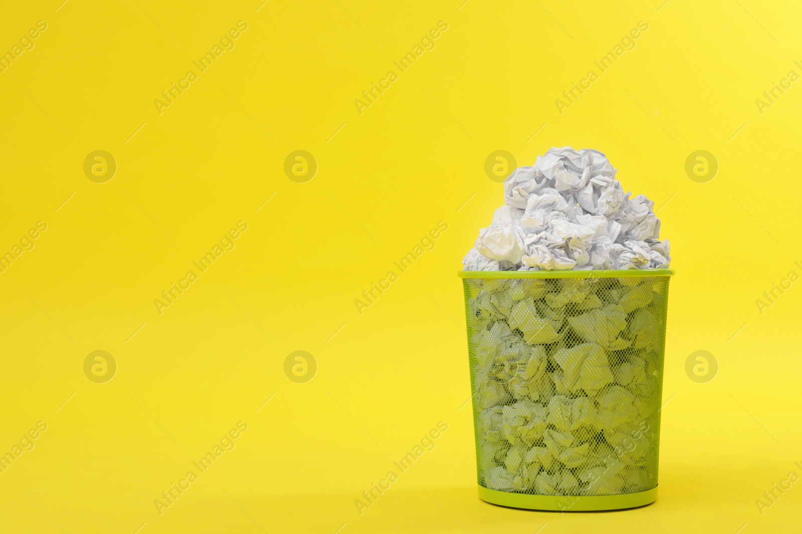 Photo of Metal bin with crumpled paper on color background, space for text