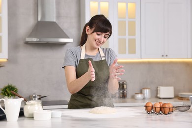 Photo of Happy young housewife making dough at white marble table in kitchen