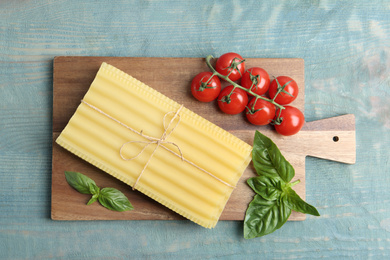 Uncooked lasagna sheets, cherry tomatoes and basil on blue wooden table, flat lay