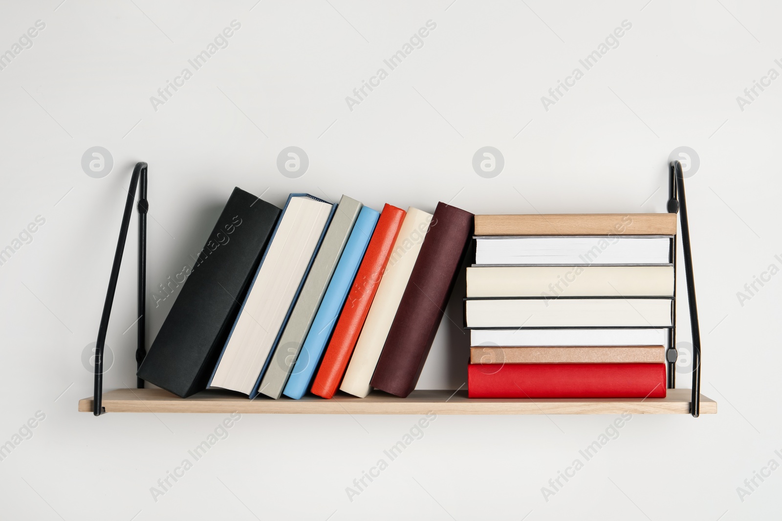 Photo of Wooden shelf with many hardcover books on white wall