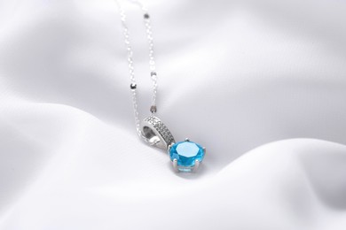 Photo of Beautiful necklace with light blue gemstone on white fabric. Luxury jewelry