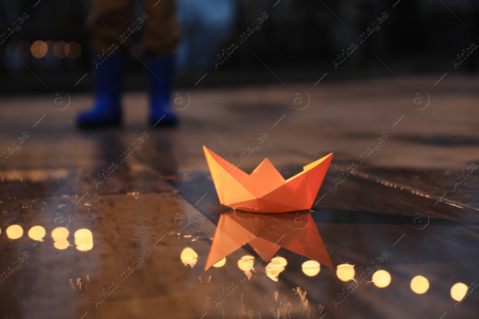 Photo of Little boy outdoors, focus on paper boat in puddle