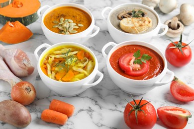 Photo of Tasty broth, different cream soups in bowls and ingredients on white marble table, closeup