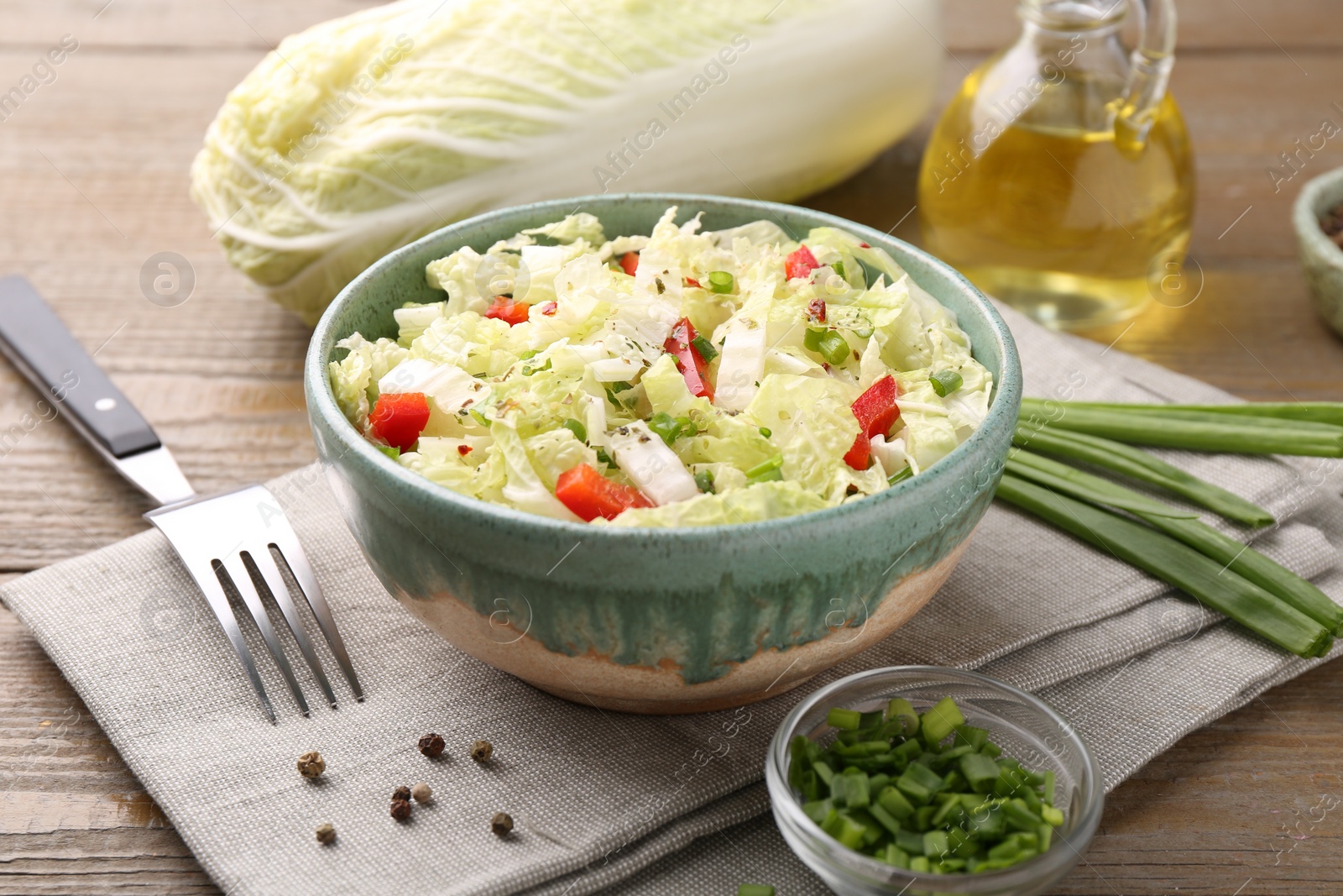 Photo of Tasty salad with Chinese cabbage in bowl, peppercorns and green onion on wooden table, closeup