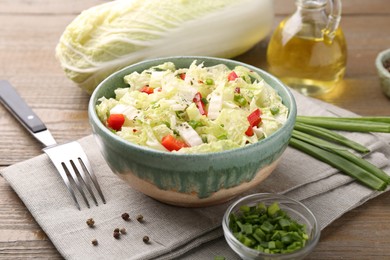 Photo of Tasty salad with Chinese cabbage in bowl, peppercorns and green onion on wooden table, closeup