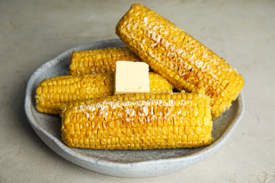 Photo of Delicious grilled corn with butter on light grey table