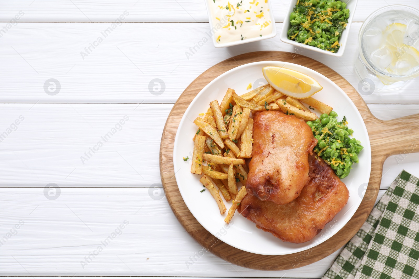 Photo of Tasty fish, chips, sauce, peas and lemon on white wooden table, top view. Space for text