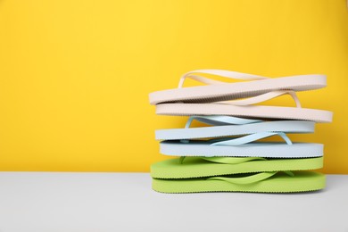 Photo of Stack of different flip flops on white table against yellow background, space for text