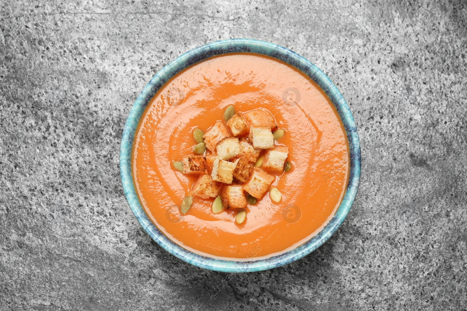 Photo of Tasty creamy pumpkin soup with croutons and seeds in bowl on grey table, top view