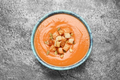 Photo of Tasty creamy pumpkin soup with croutons and seeds in bowl on grey table, top view