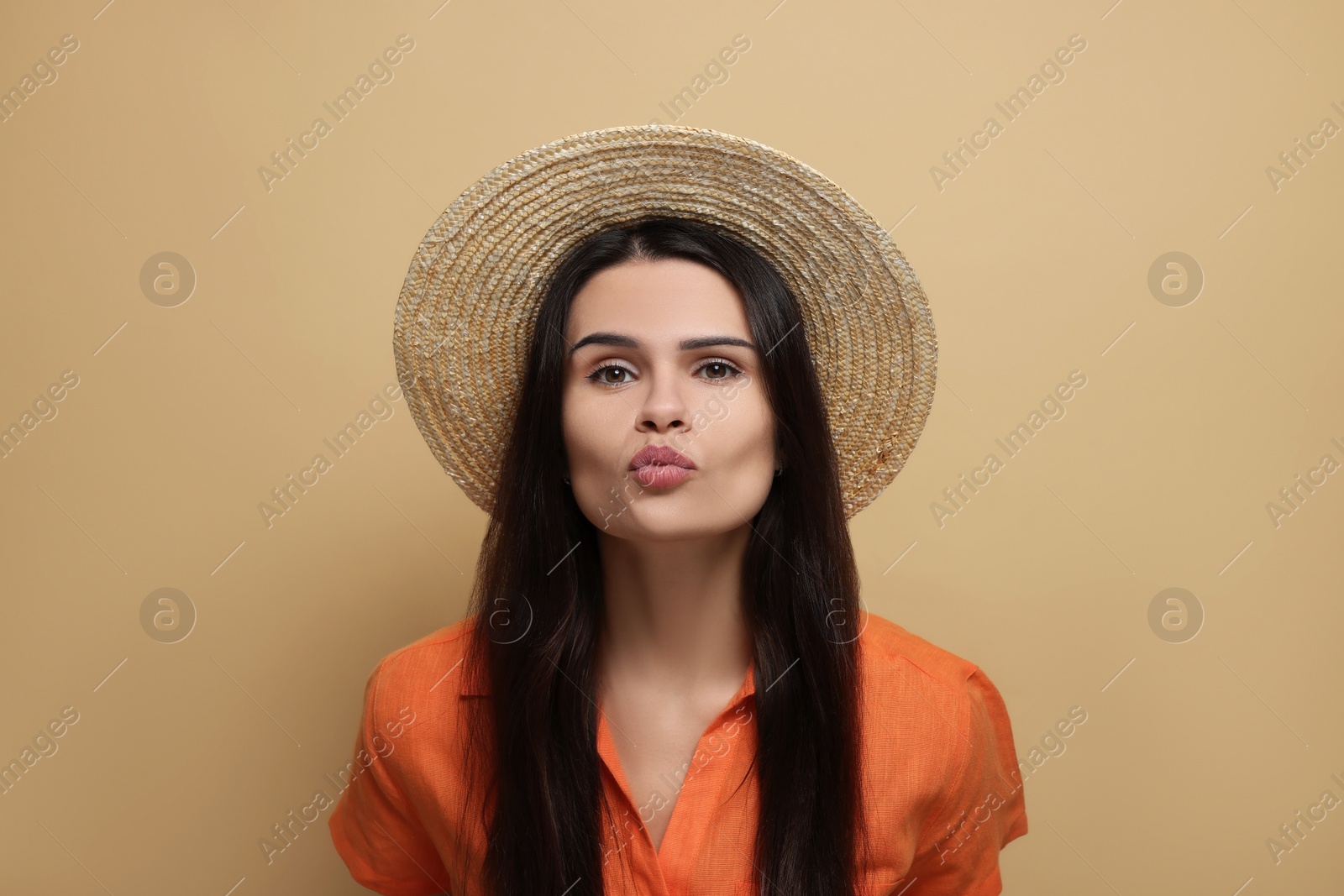 Photo of Beautiful young woman in straw hat giving kiss on beige background