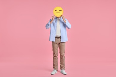 Man holding emoticon with closed eyes and mouth on pink background