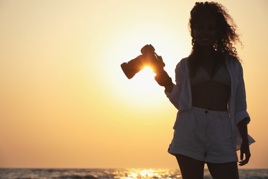 Photo of African American photographer with professional camera near sea at sunset