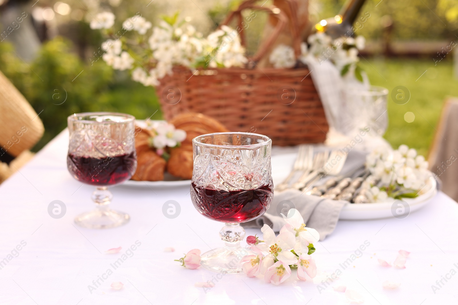 Photo of Stylish table setting with beautiful spring flowers, wine and croissants in garden