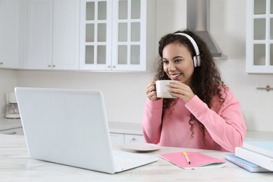 Photo of African American woman drinking tea while studying in kitchen at home. Distance learning
