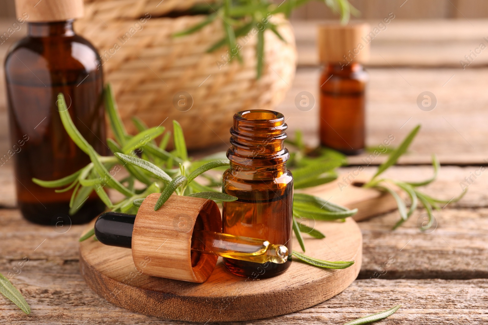 Photo of Aromatic essential oils in bottles, pipette and rosemary on wooden table, closeup