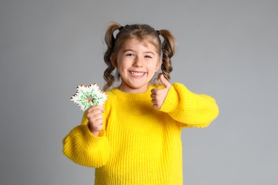 Cute little girl with Christmas gingerbread cookie on light grey background