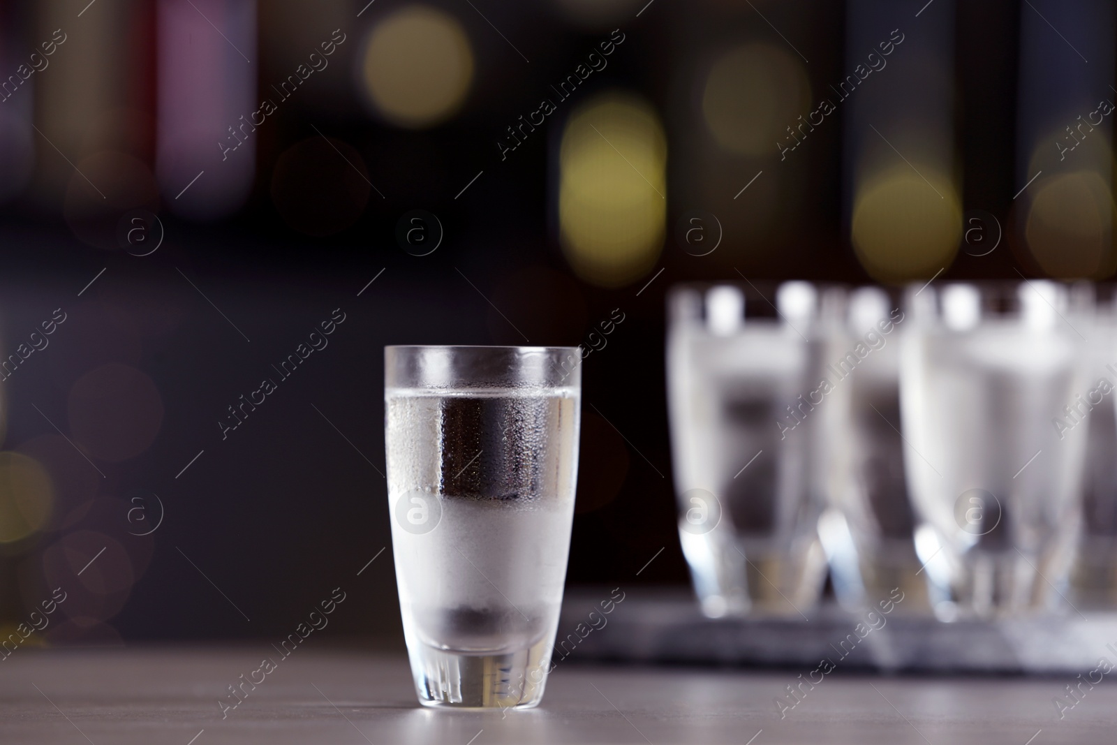 Photo of Shot of vodka on table against blurred background