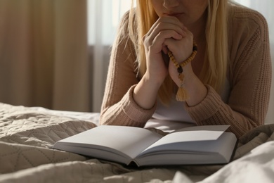 Religious young woman praying over Bible in bedroom