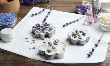 Photo of Handmade soap bars with lavender flowers in metal forms and ingredients on brown wooden table