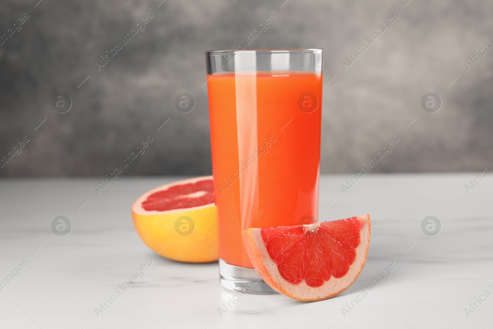 Photo of Tasty grapefruit juice in glass and fresh fruit on white table