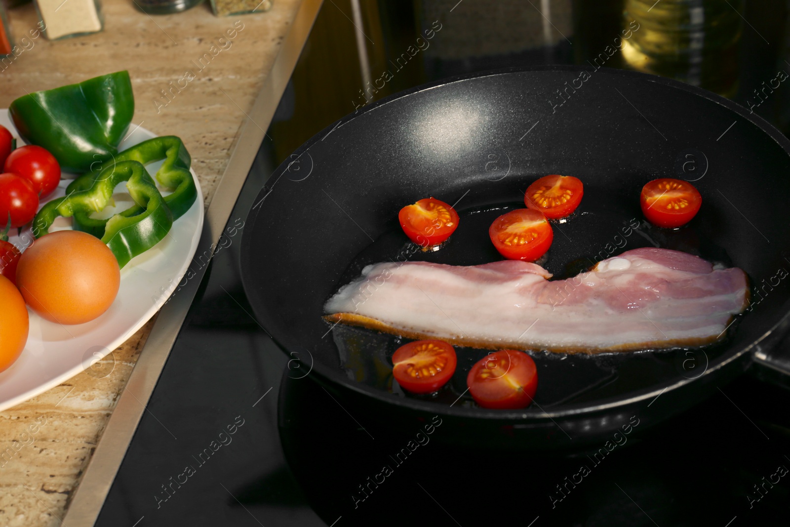 Photo of Cooking bacon with tomatoes in frying pan. Ingredients for breakfast