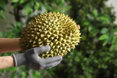 Photo of Woman in gloves holding fresh ripe durian outdoors, closeup