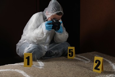Photo of Criminologist in protective suit working at crime scene outdoors