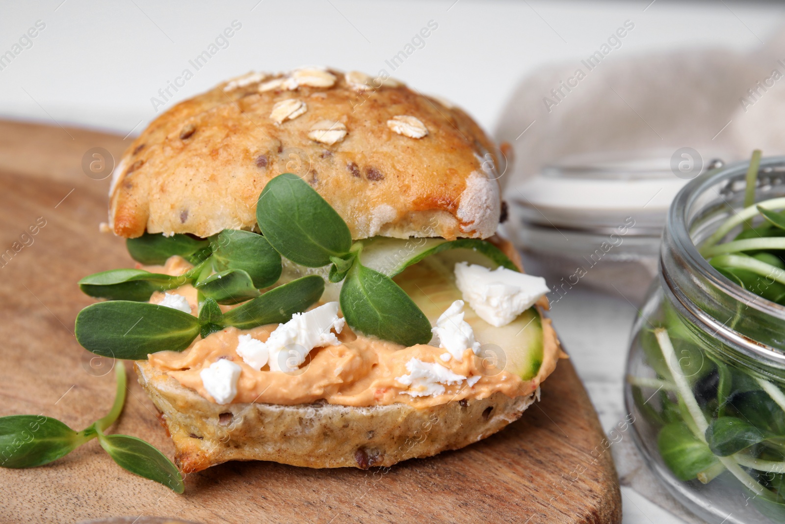 Photo of Delicious sandwich with hummus, microgreens and cucumber slices on wooden board, closeup