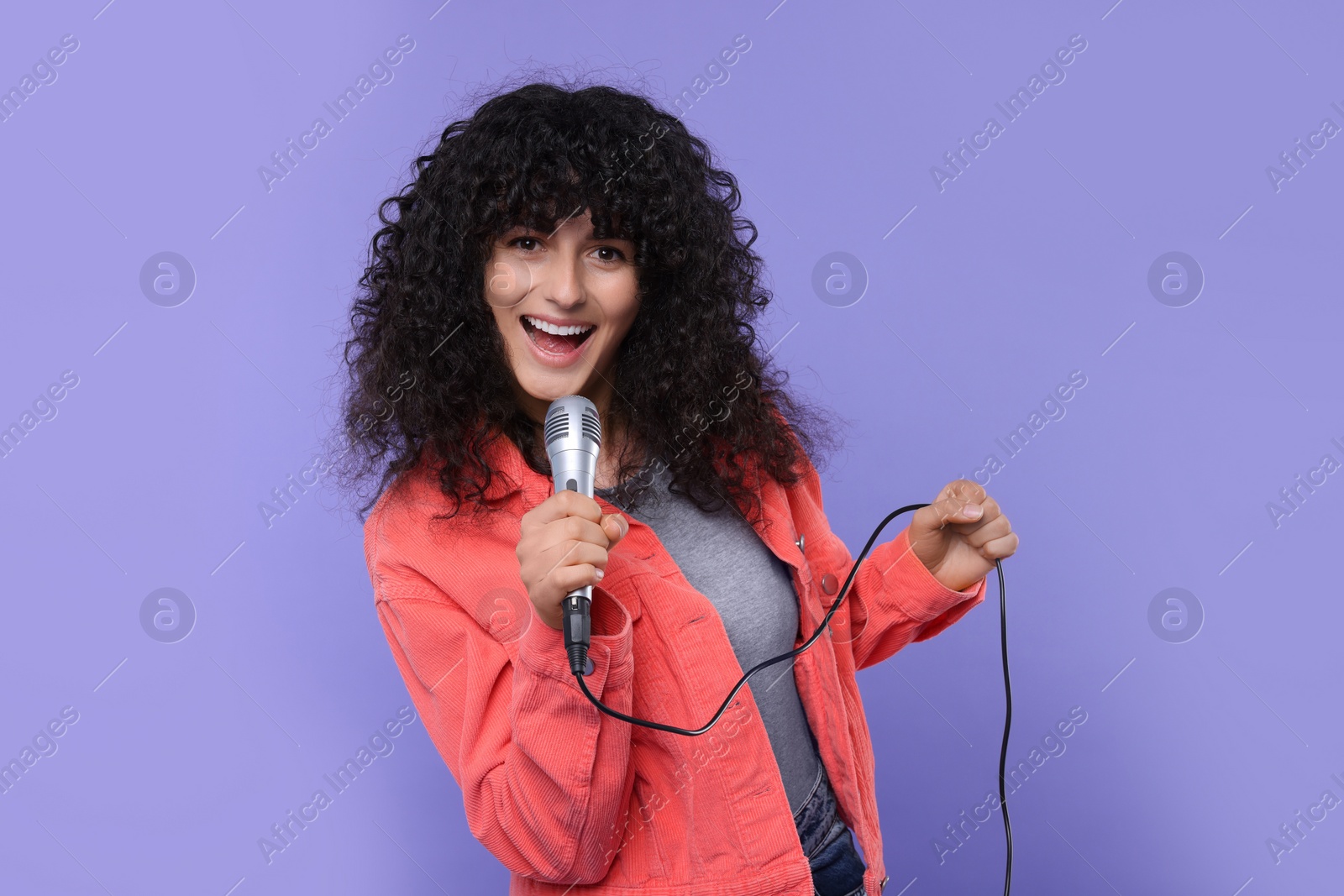 Photo of Beautiful young woman with microphone singing on purple background