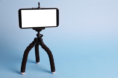 Modern tripod with smartphone on light blue background. Space for text