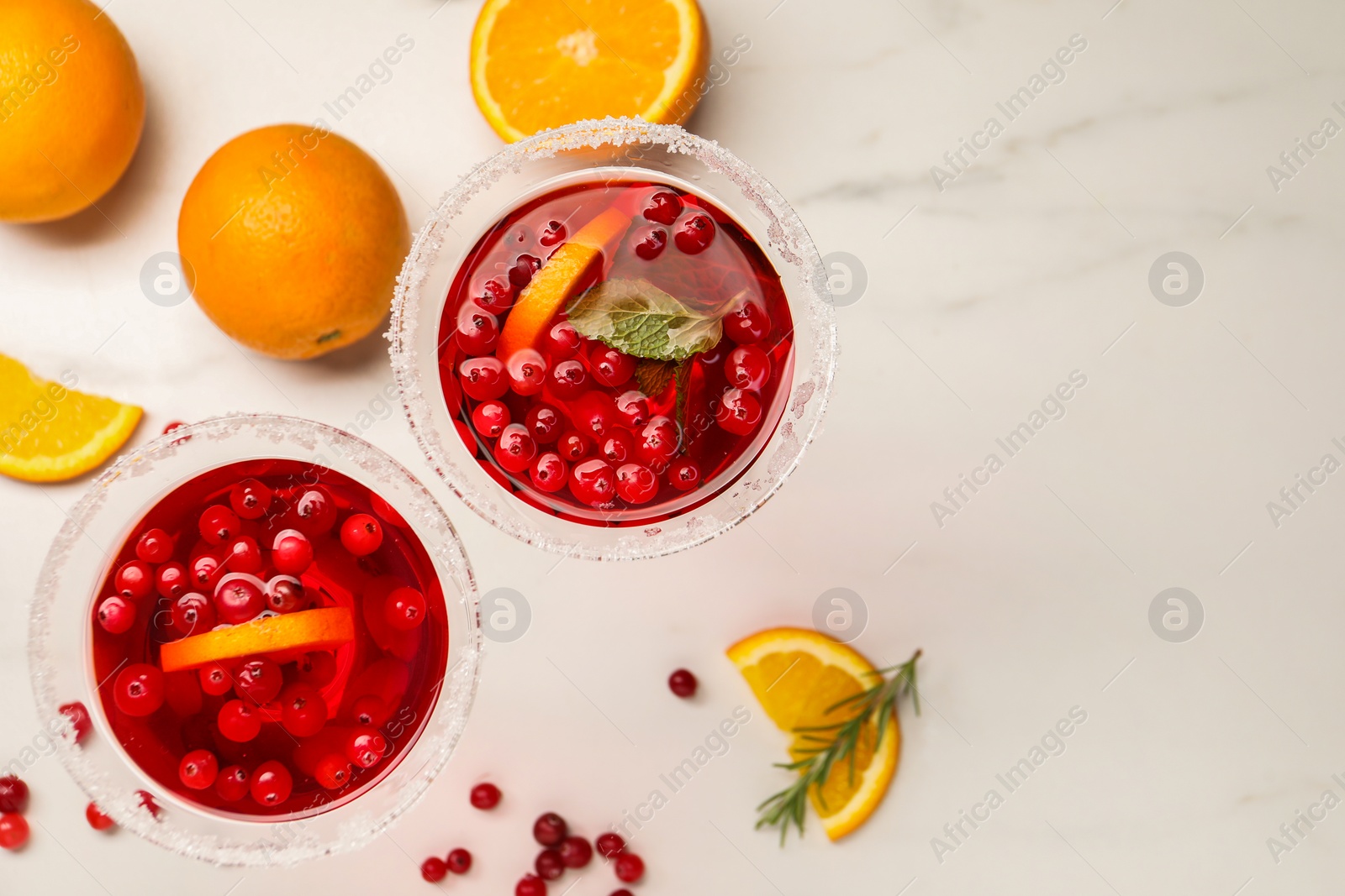 Photo of Tasty cranberry cocktail with rosemary and oranges in glasses on white table, flat lay. Space for text