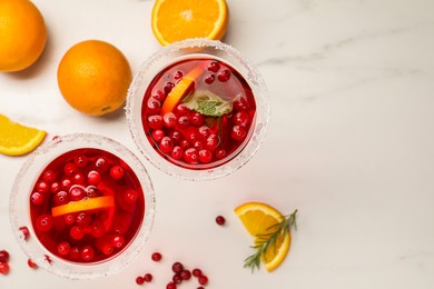 Tasty cranberry cocktail with rosemary and oranges in glasses on white table, flat lay. Space for text
