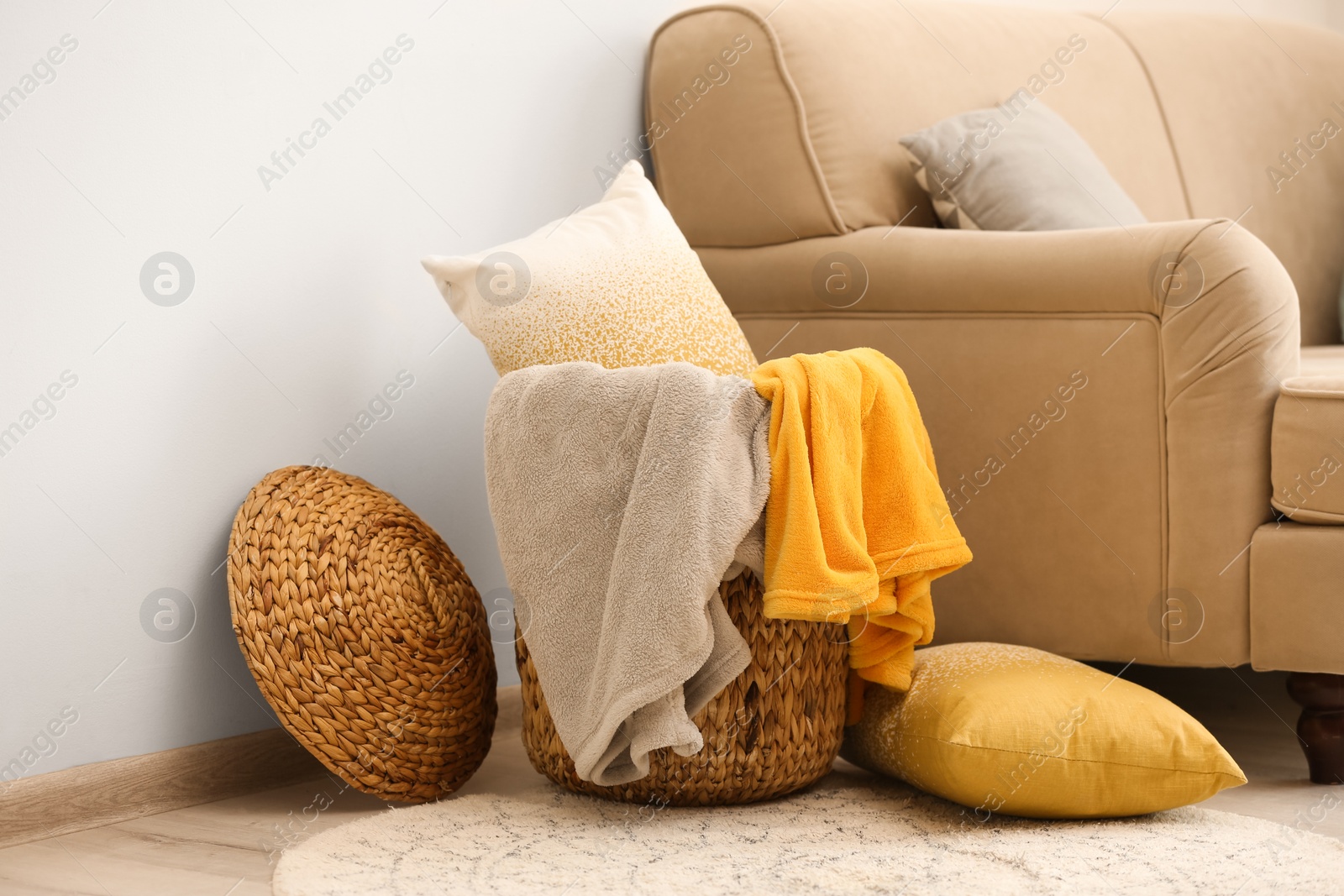 Photo of Wicker basket with color blankets and pillows near beige sofa, space for text. Idea for interior design