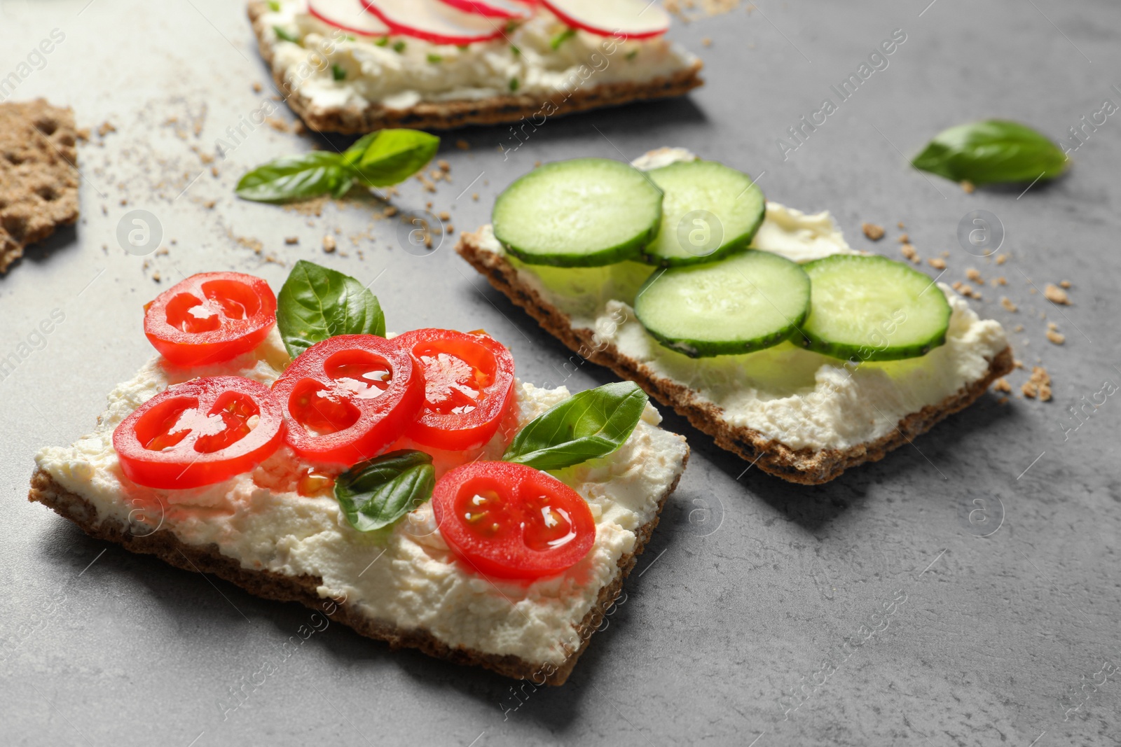 Photo of Tasty snacks with cream cheese and vegetables on gray table