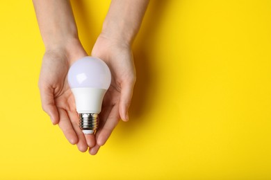 Photo of Woman holding light bulb on yellow background, top view. Space for text