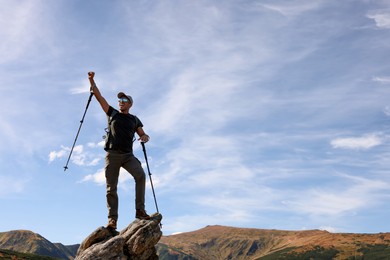 Man with backpack and trekking poles on rocky peak in mountains