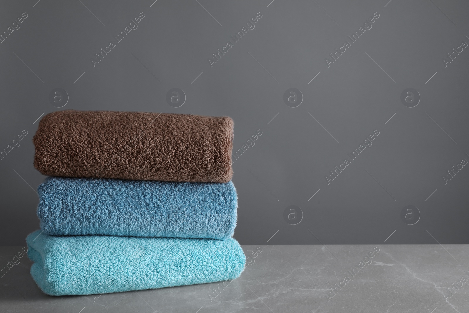 Photo of Stack of clean bath towels on grey table. Space for text