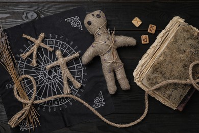Photo of Voodoo doll with pins surrounded by ceremonial items on black wooden table, flat lay