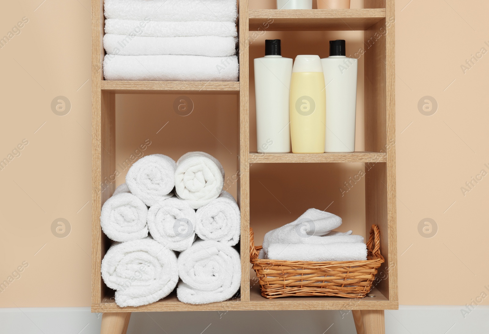 Photo of Soft folded towels and cosmetic bottles on wooden shelving unit near beige wall