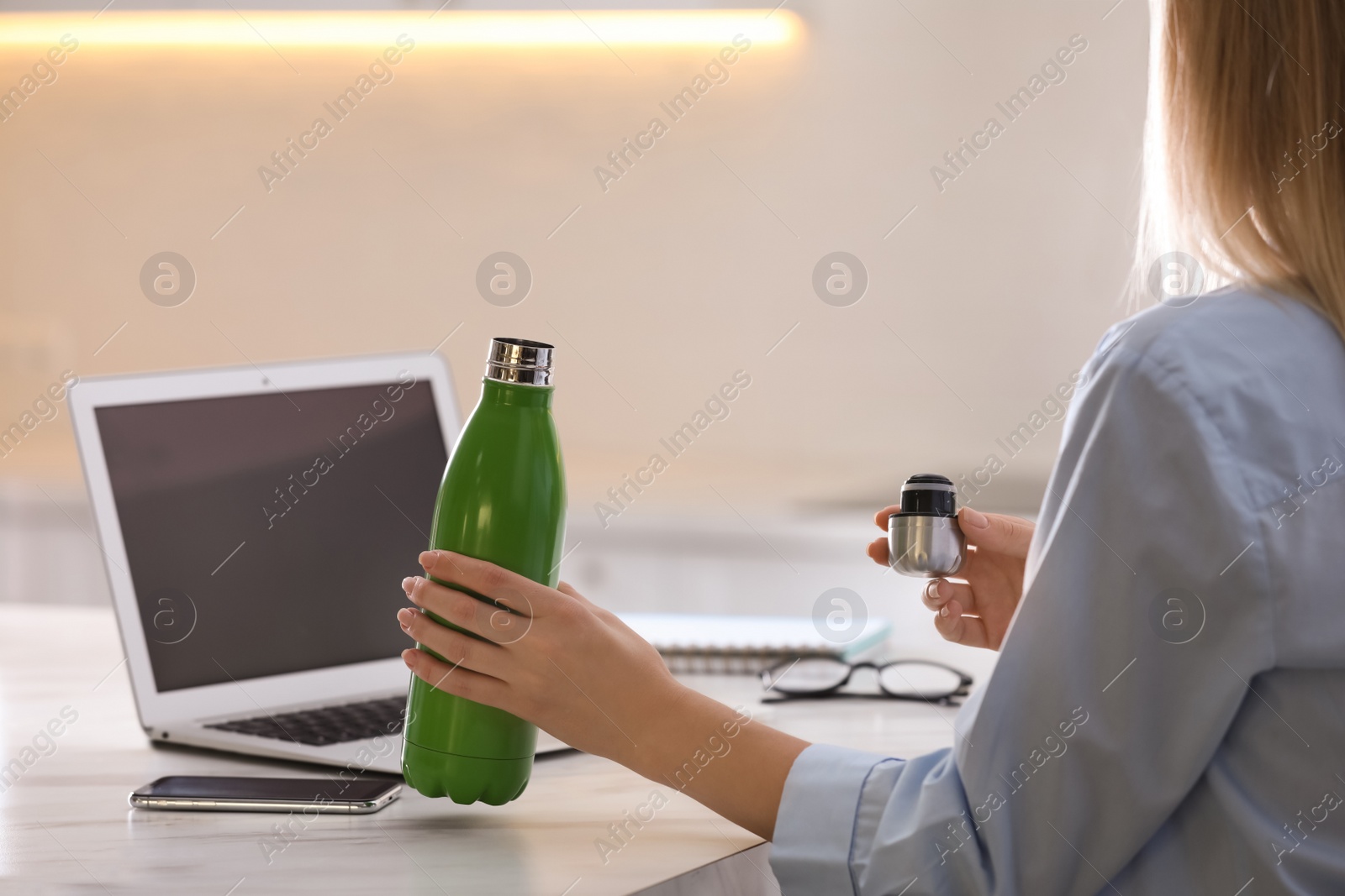 Photo of Woman with thermo bottle working at table in modern office, closeup