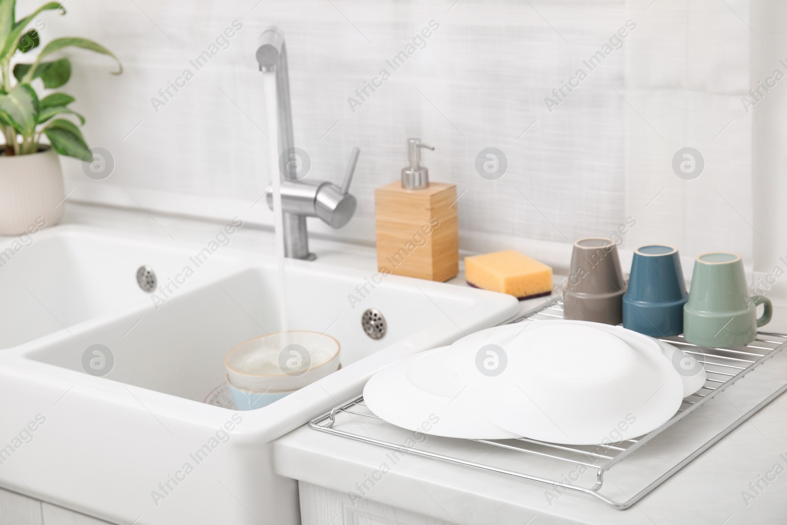 Photo of Drying rack with clean dishes near sink in stylish kitchen