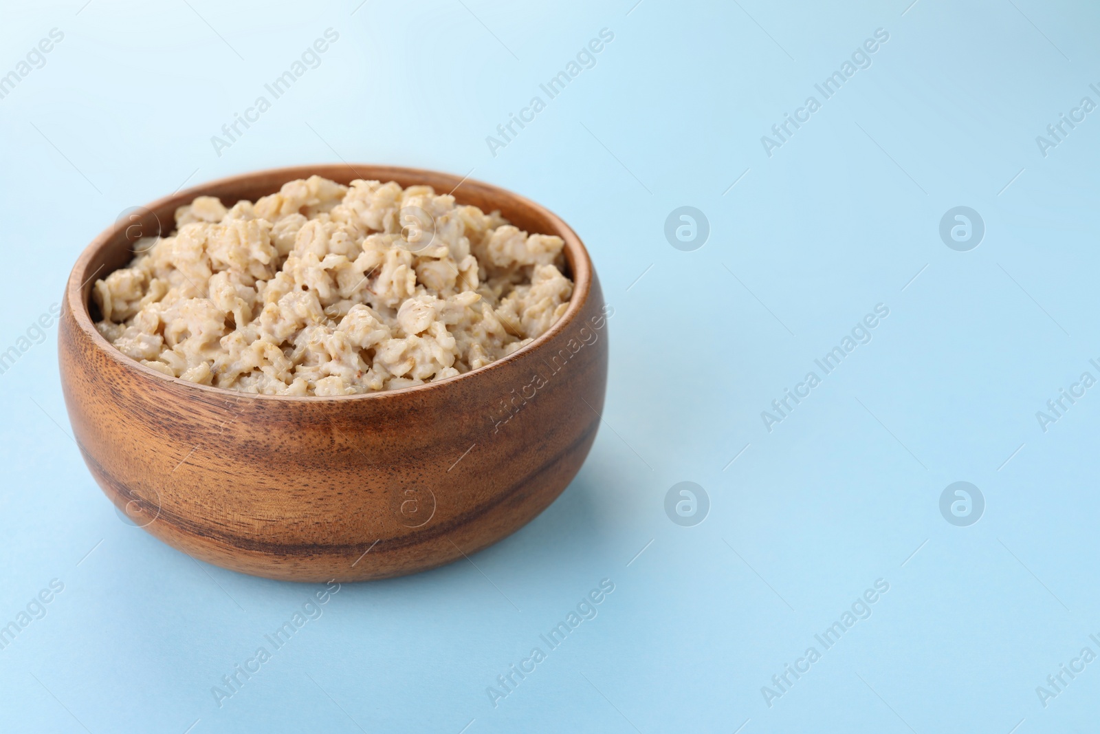 Photo of Tasty boiled oatmeal in bowl on light blue background, space for text