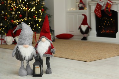 Photo of Funny Christmas gnomes and candle holder on floor in room with festive decoration. Space for text