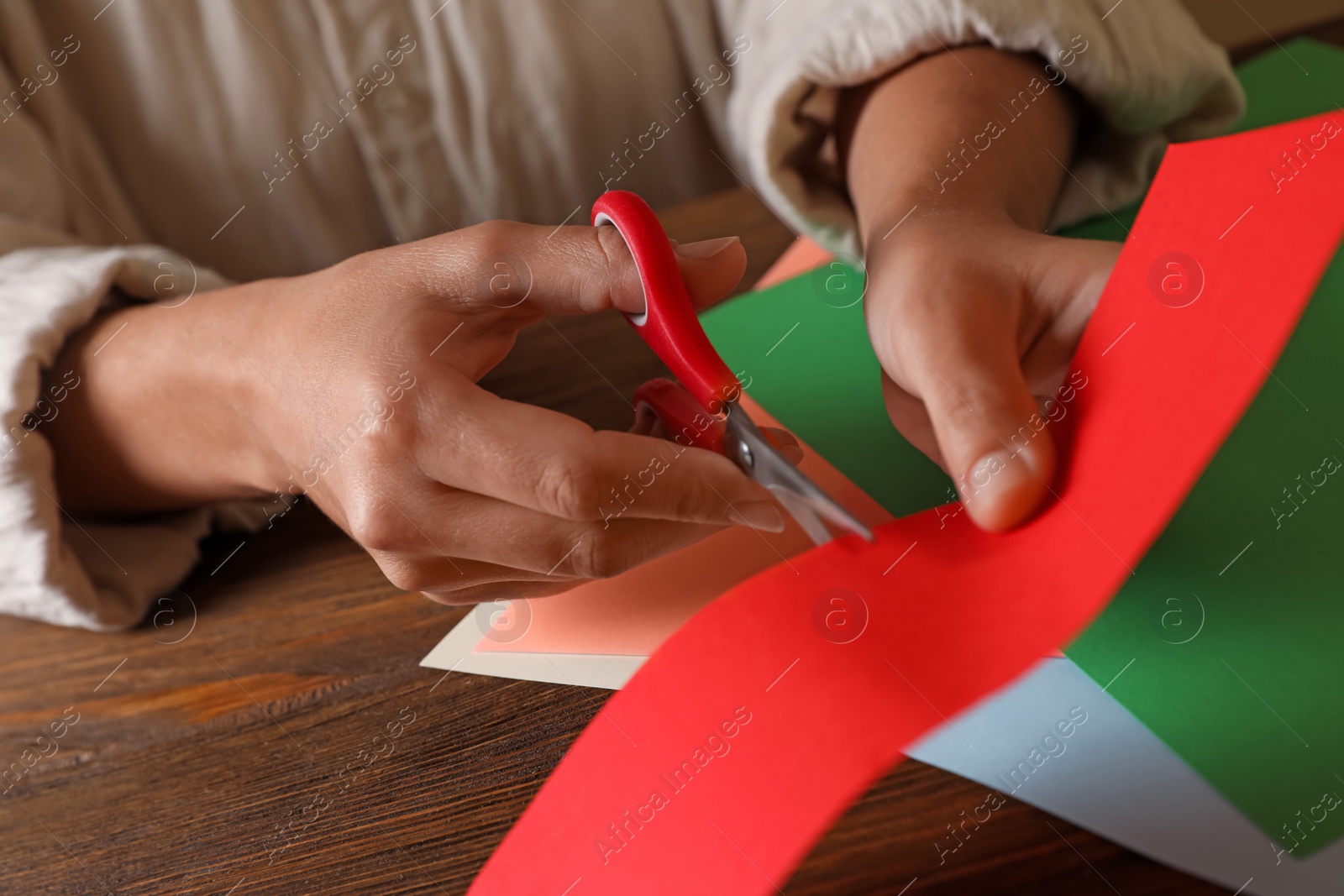 Photo of Woman cutting red paper with scissors at wooden table, closeup