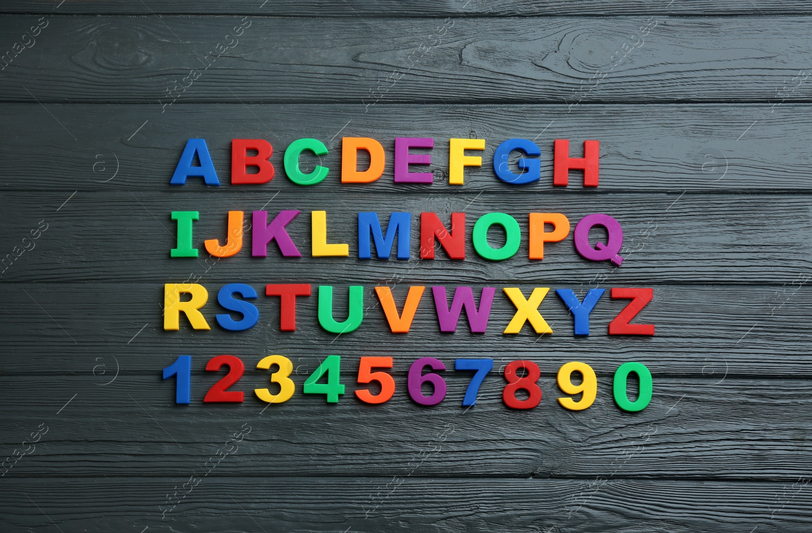 Photo of Colorful magnetic letters and numbers on black wooden background, flat lay