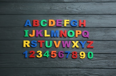 Colorful magnetic letters and numbers on black wooden background, flat lay