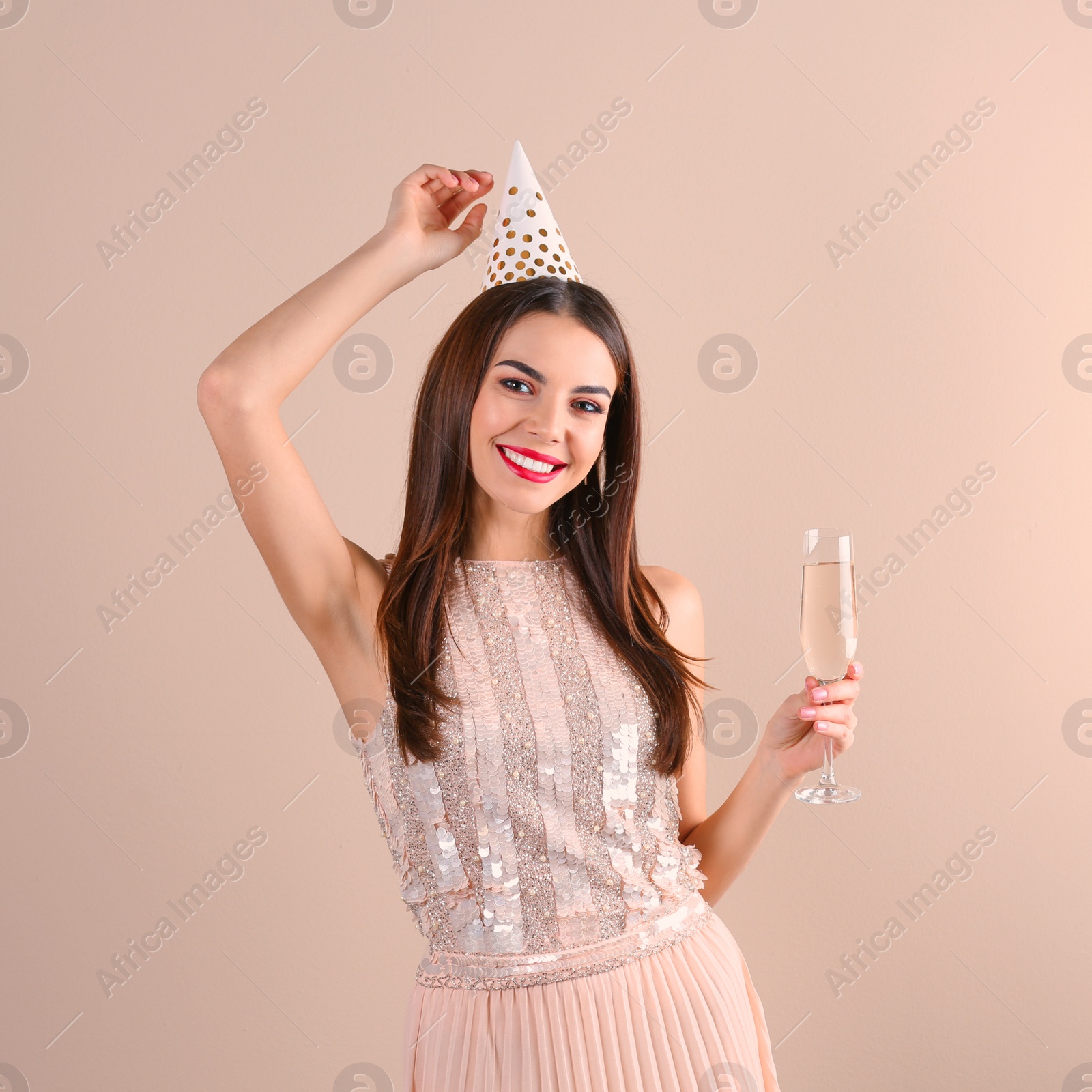 Photo of Portrait of happy woman with party hat and champagne in glass on color background