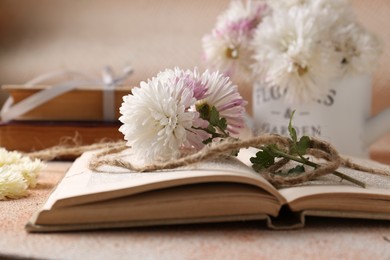 Book with chrysanthemum flowers as bookmark on beige textured table, closeup